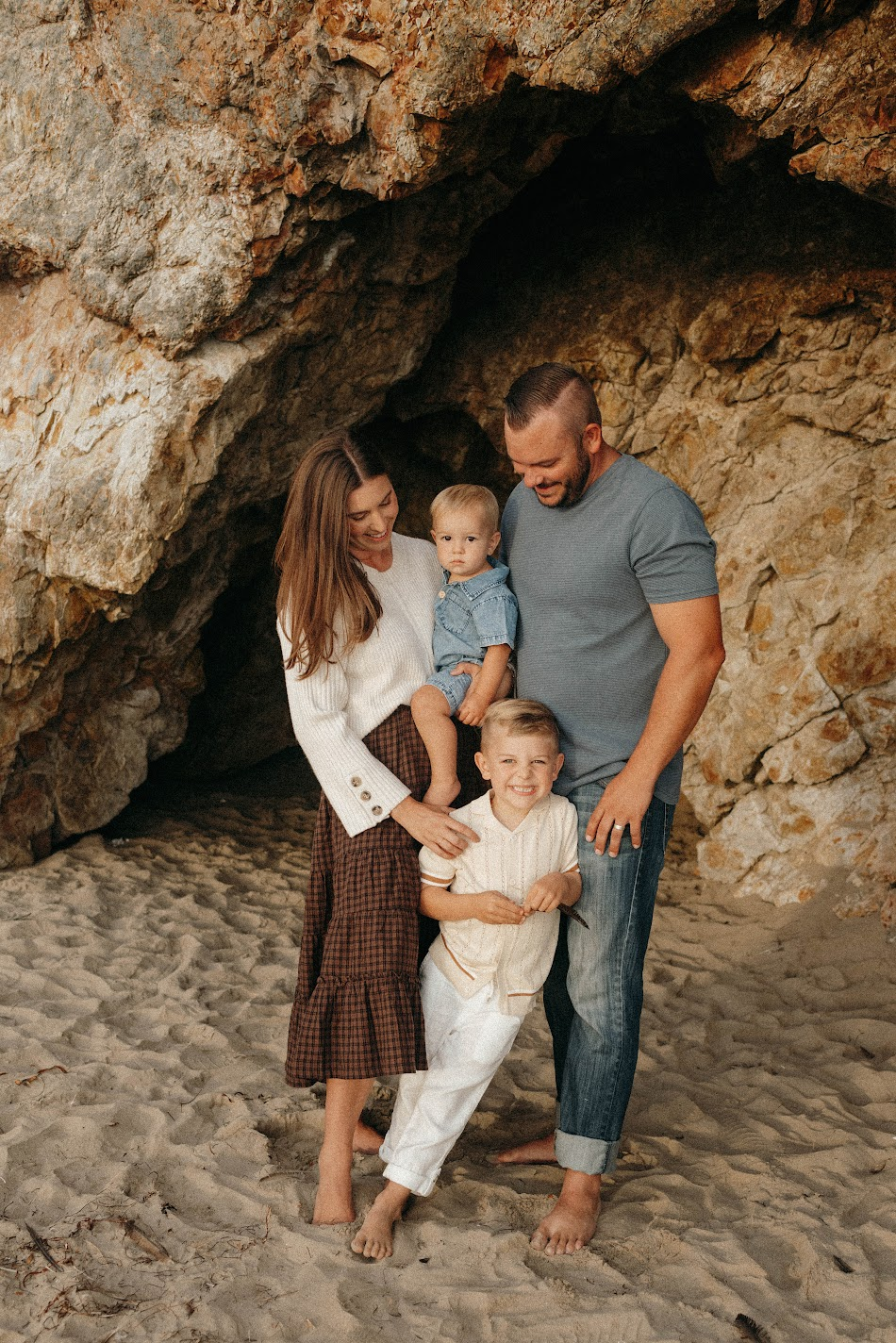 Family of four with two young boys nestled inside a sandstone sea cave