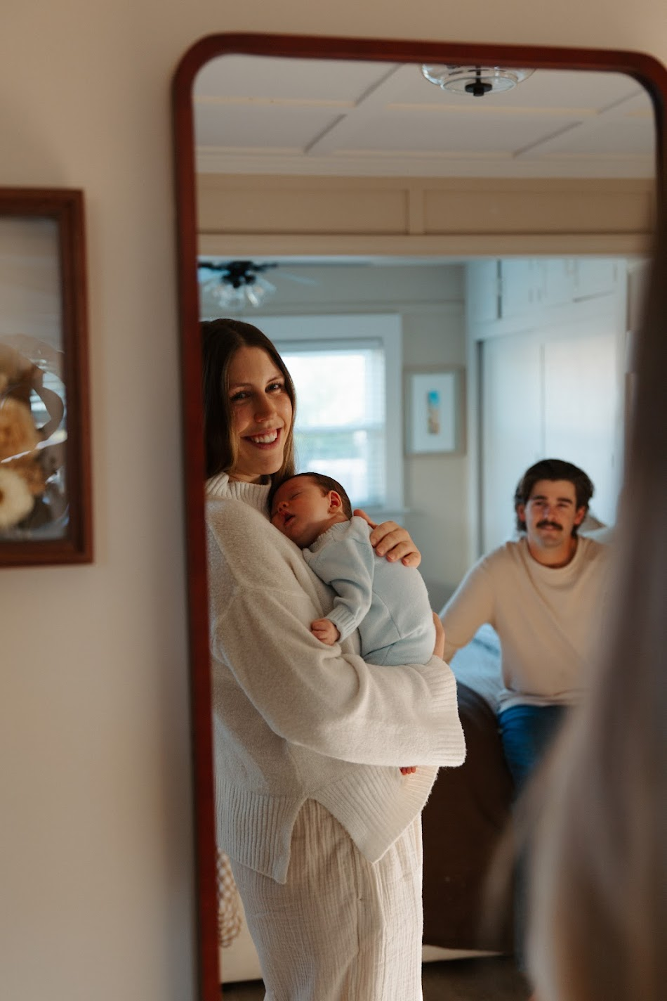 Mirror reflection of a smiling mother holding her newborn with father seated behind