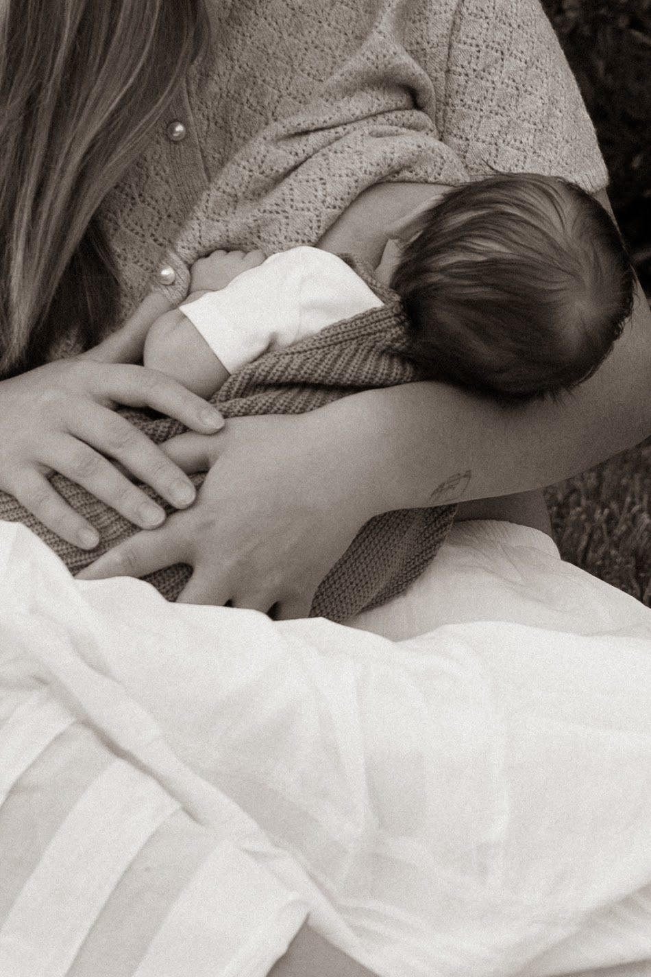 Sepia close-up of a mother cradling her swaddled newborn outdoors