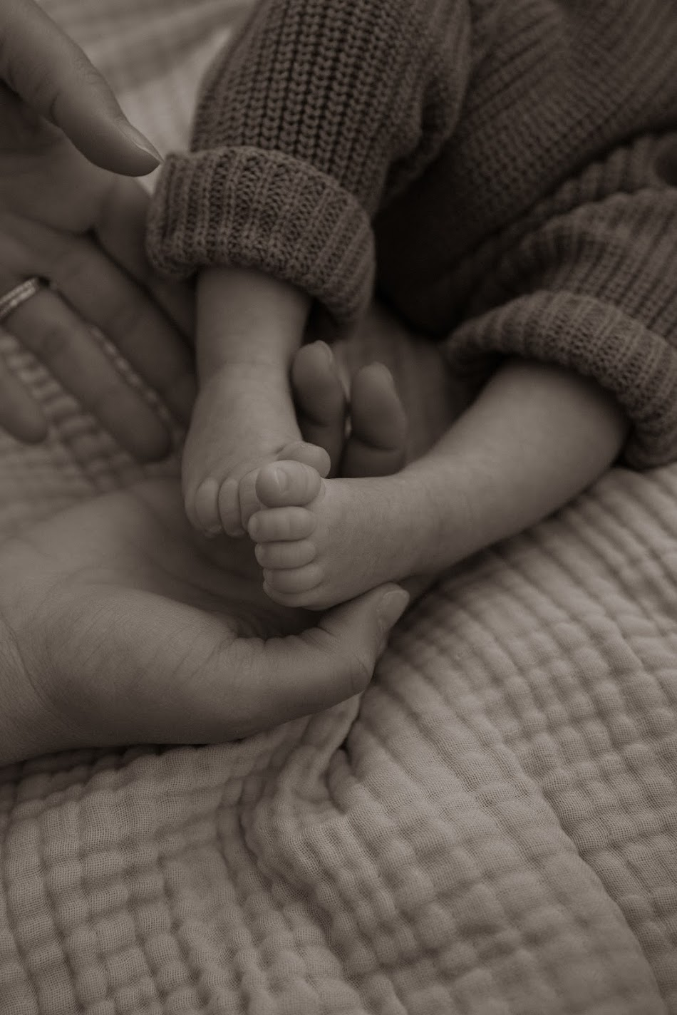 Sepia close-up of a newborn's tiny feet held in a parent's hands