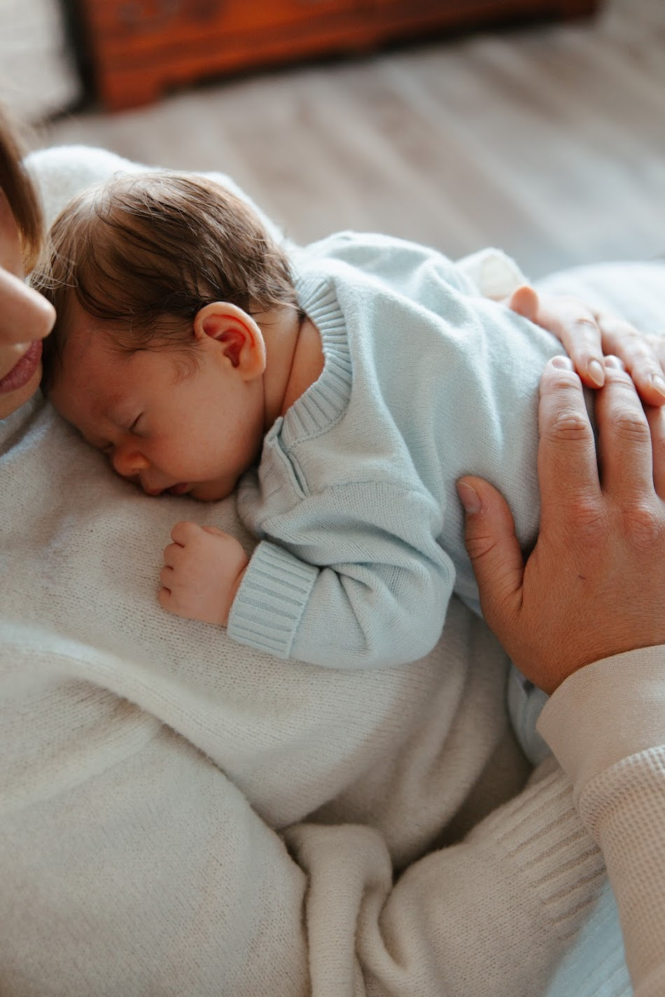 Newborn in a soft blue knit sweater sleeping on a parent's chest