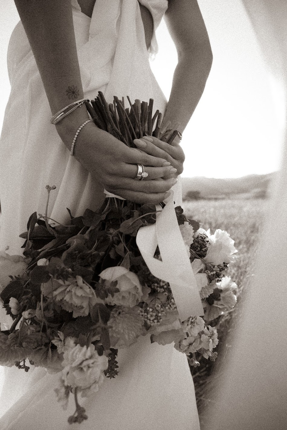 Black and white close-up of a bride's hands and ring holding a wild garden bouquet