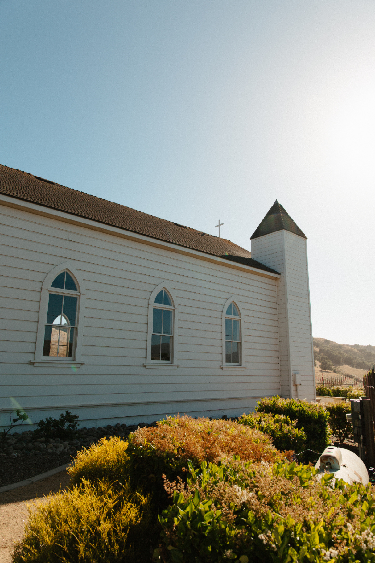 Sunlit white wooden chapel with arched windows and steeple set against golden hills