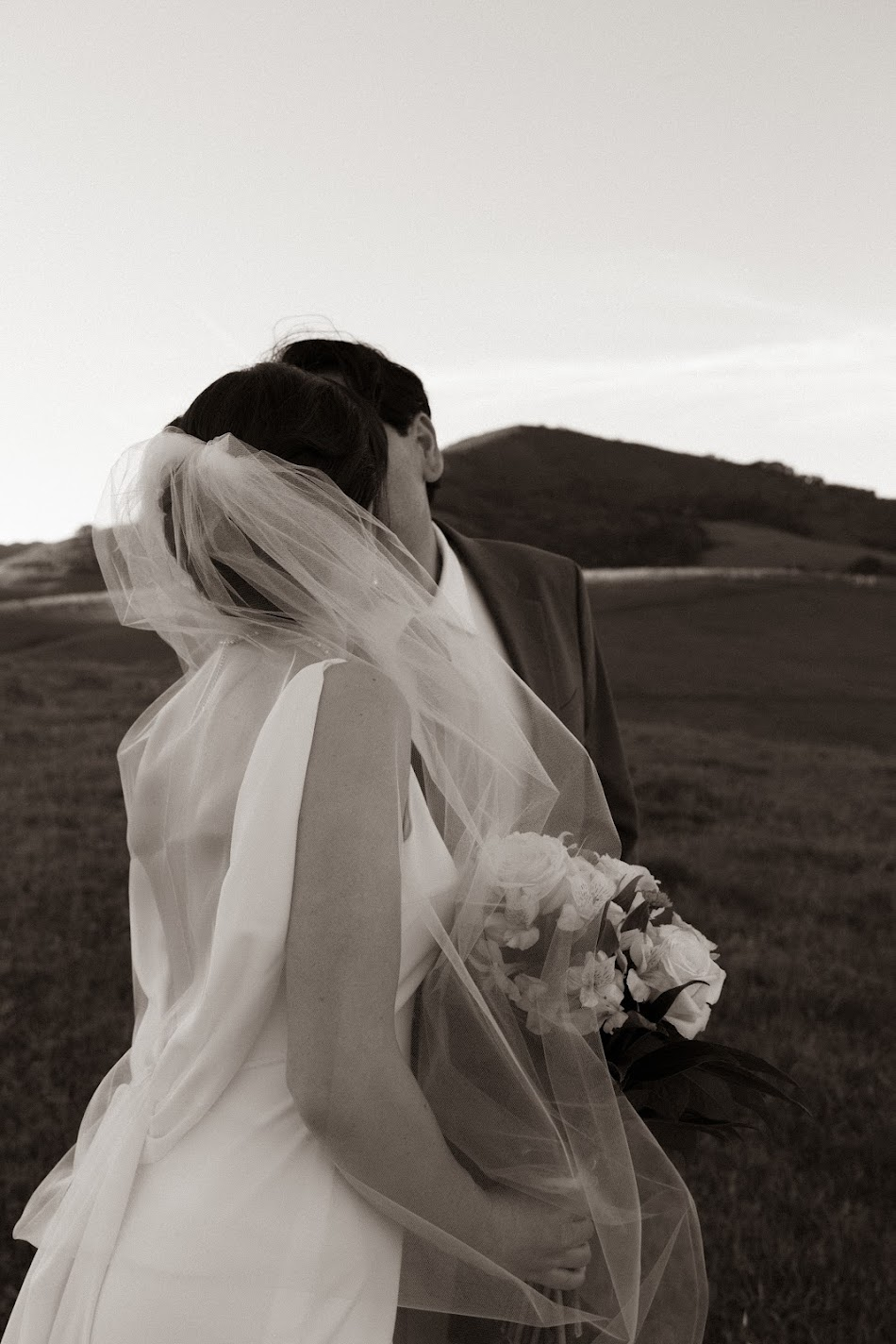 Sepia embrace of a bride and groom with flowing veil in rolling hills